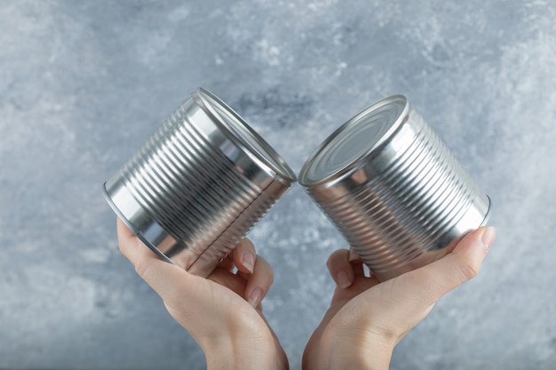 Woman hands holding two metallic cans on marble.