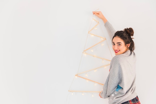 Free photo woman hanging wooden christmas tree on wall