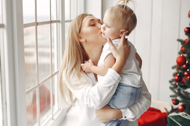 Woman has fun preparing for Christmas. Mother in a white shirt is playing with her daughter. Family is resting in a festive room.