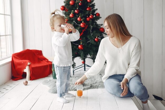 Woman has fun preparing for Christmas. Mother in white sweater playing with daughter. Family is resting in a festive room.