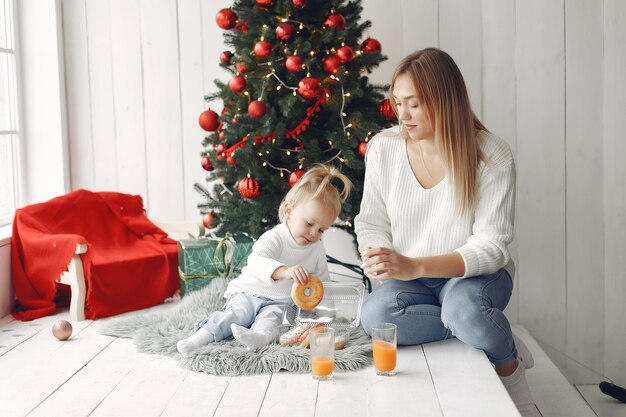 Woman has fun preparing for Christmas. Mother in white sweater playing with daughter. Family is resting in a festive room.