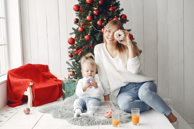 Woman has fun preparing for Christmas. Mother in white sweater playing with daughter. Family is resting in a festive room.