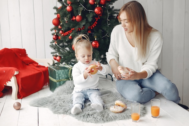 Woman has fun preparing for Christmas. Mother in white sweater playing with daughter. Family is resting in a festive room.