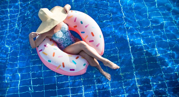 A woman in a hat relaxes on an inflatable circle in the pool.