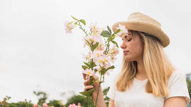 Woman in hat smelling light flowers