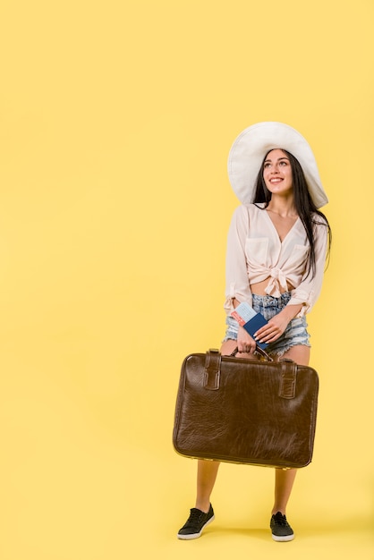 Woman in hat standing and holding suitcase 