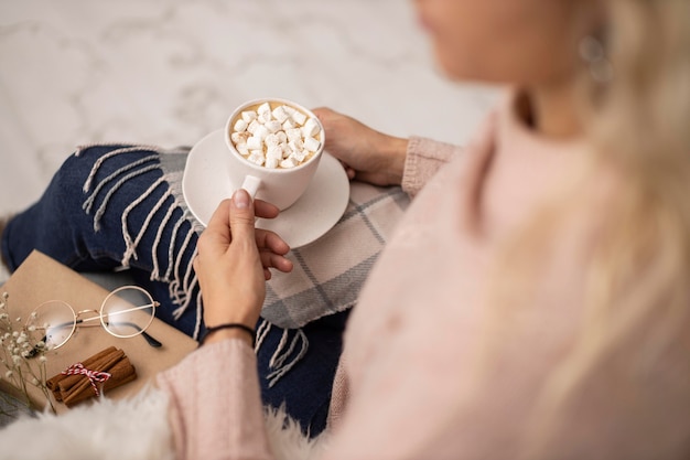 Free photo woman having cup of hot cocoa with marshmallows while reading