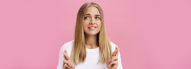 Free photo woman having dream wanting desire come true crossing fingers for good luck making wish biting lower lip while daydreaming about thing she wants buy looking aside posing over pink background