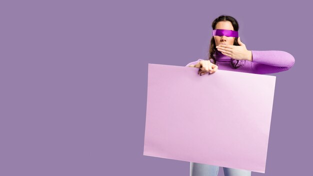 Woman having her eyes tied holding an empty cardboard and does not speak