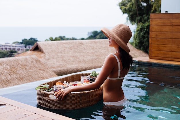 Woman having tropical healthy breakfast at villa on floating table