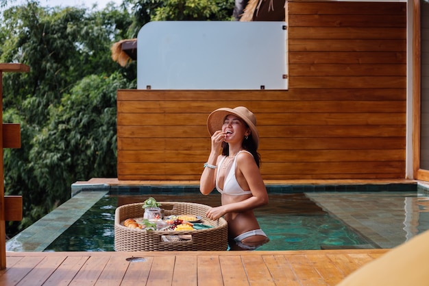 Free photo woman having tropical healthy breakfast at villa on floating table