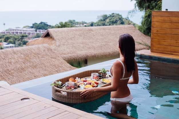 Free photo woman having tropical healthy breakfast at villa on floating table