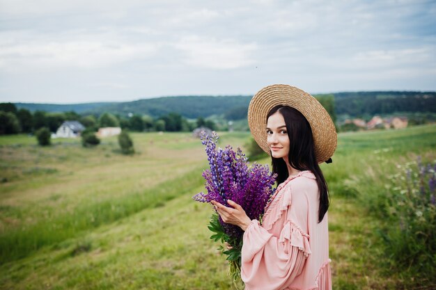 Woman in hay hat poses with bouquet of lavander on the field 