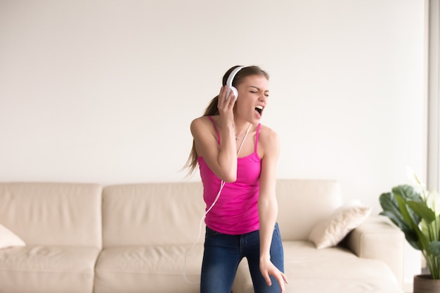 Woman in headphones singing and dancing at home