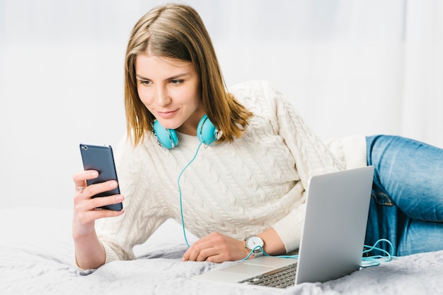 Woman in headphones using smartphone near laptop