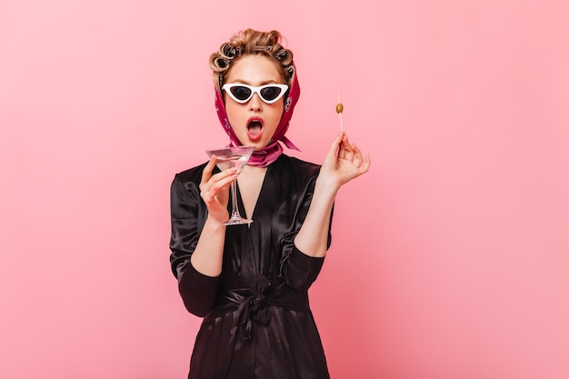 Free photo woman in headscarf and robe in amazement looks at front holding olive and martini glass