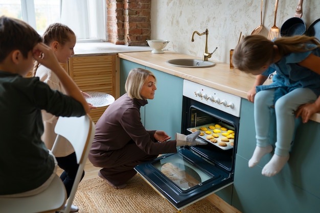 Free photo woman helping kids bake cookies side view