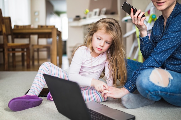 Free photo woman and her child sitting on carpet with cellphone and laptop