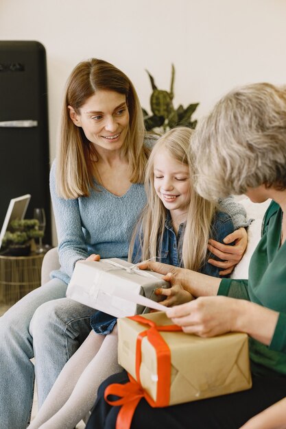 Woman, her mother and her daughter sitting on a couch. Girl keep a box with present.