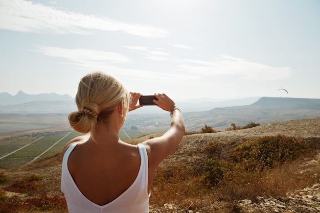 Woman hiker taking photo with smartphone on mountain peak