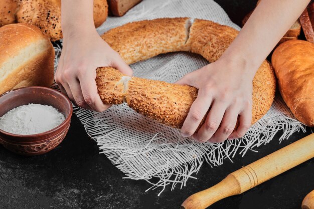 Woman holding bagel on dark table with various bread.