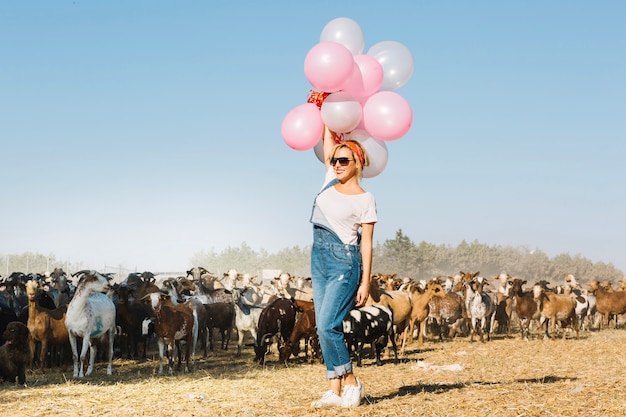 Woman holding balloons over head near goats