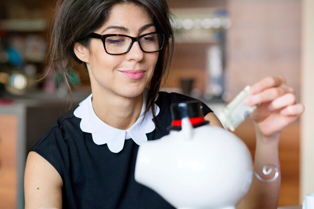 Woman holding a bill next to a piggy bank