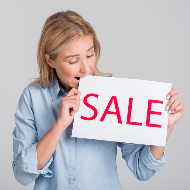 Free photo woman holding and biting from sale sign