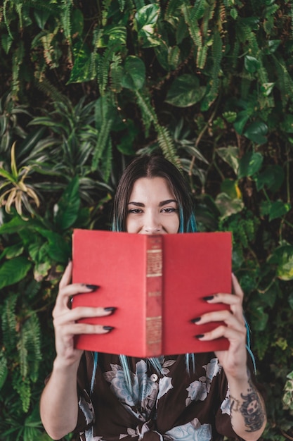 Free photo woman holding book in front of her mouth standing against plant