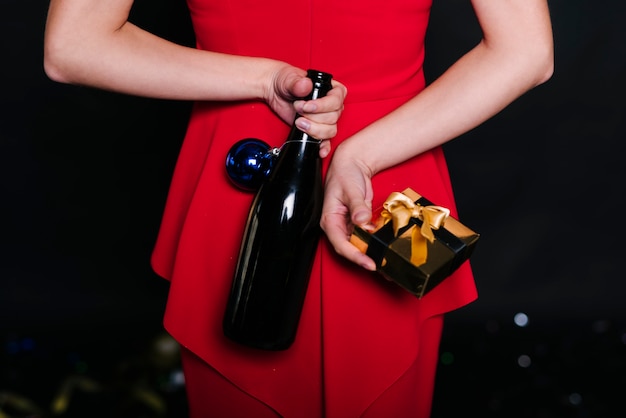 Woman holding bottle with gift box behind back 