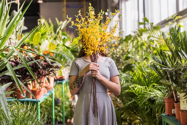 Woman holding bunch of twigs near face between green plants