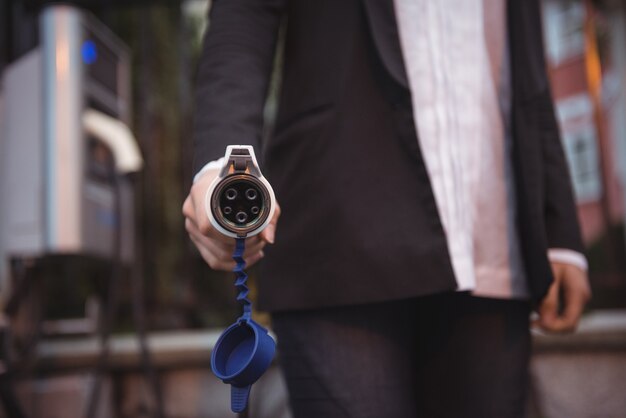 Woman holding car charger at electric vehicle charging station