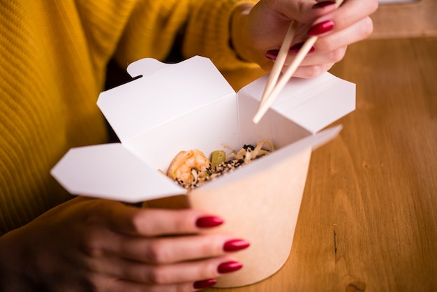 Woman holding chopsticks and box of noodles