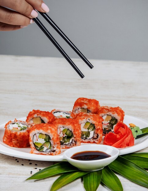 woman holding chopsticks to take sushi rolls with red tobiko