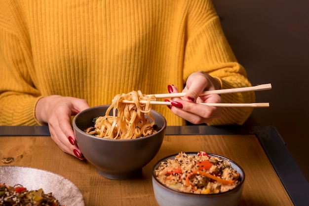 Woman holding chopsticks with noodles at table