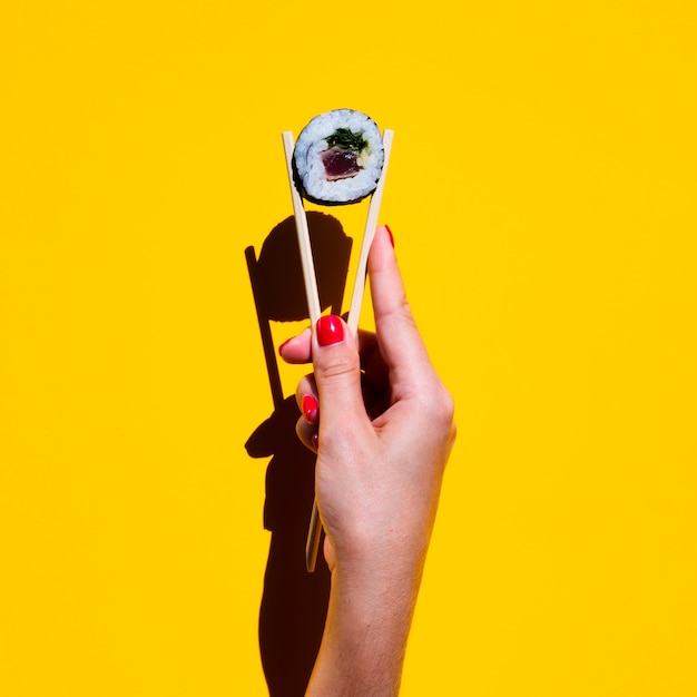 Free Photo woman holding chopsticks with sushi roll on yellow background