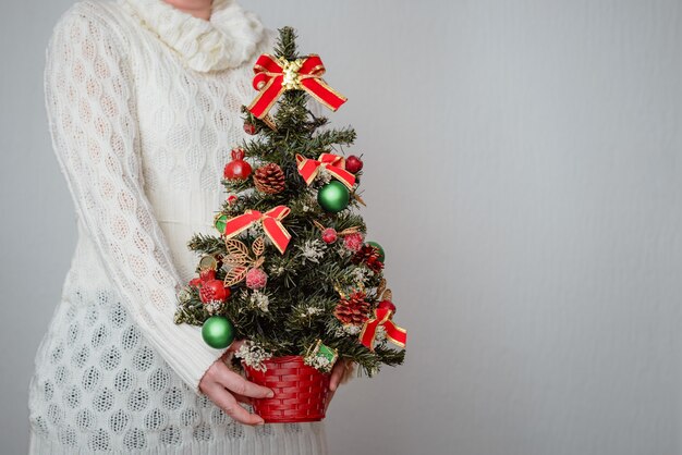 Free photo woman holding a christmas tree on grey wall