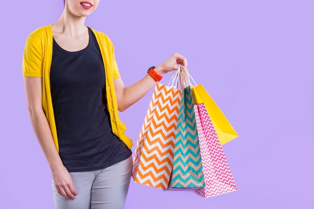 Free photo woman holding colorful paper shopping bag against purple wallpaper