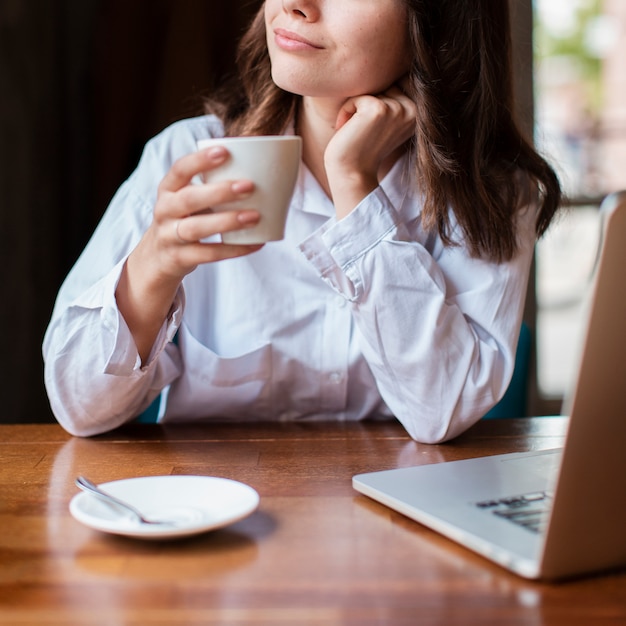 Free photo woman holding a cup of coffee with laptop on desk