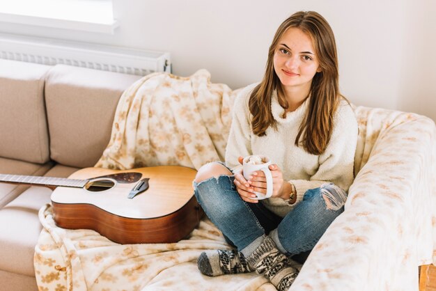 Woman holding cup near guitar on sofa