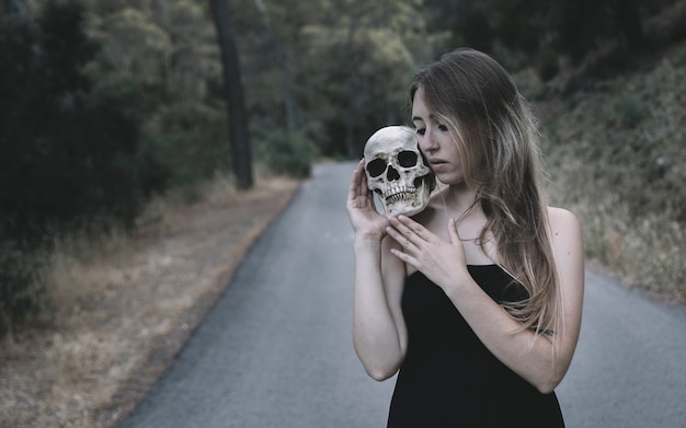 Woman holding a decorative human skull on shoulder standing on road