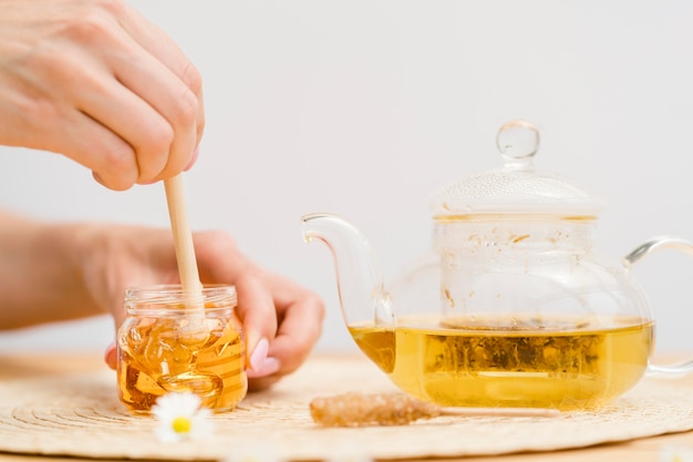 Woman holding dipper in honey jar near teapot