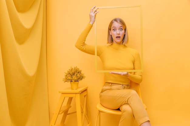 Woman holding frame around face in a yellow scene