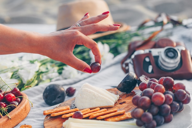 Free Photo woman holding fruit with cheese and fruits on wooden cutting board and camera, hat and flowers in beach.