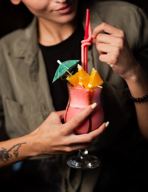 Free photo woman holding a glass of pink cocktail garnished with orange slices