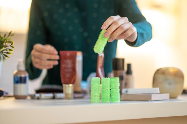 Woman holding green curlers in hands during online tutorial on hairstyling