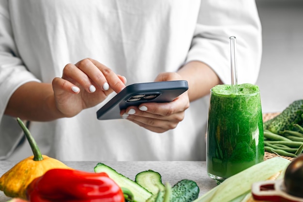 Free Photo a woman holding a green detox smoothie and using nutrition app on smartphone