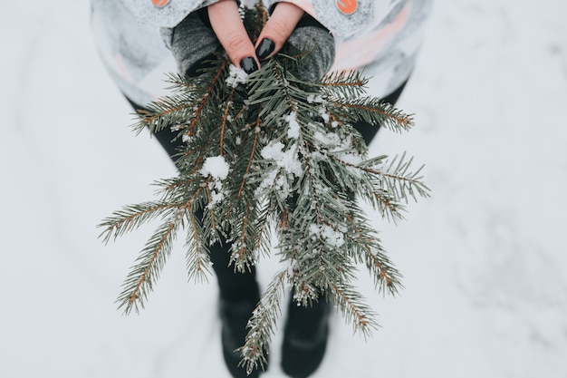 Woman holding green pine branches with snow on blurred background