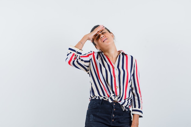 woman holding hand over eyes in shirt, skirt and looking tired.