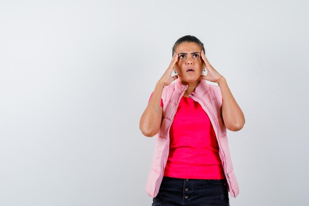 Woman holding hands to head in t-shirt, vest and looking helpless